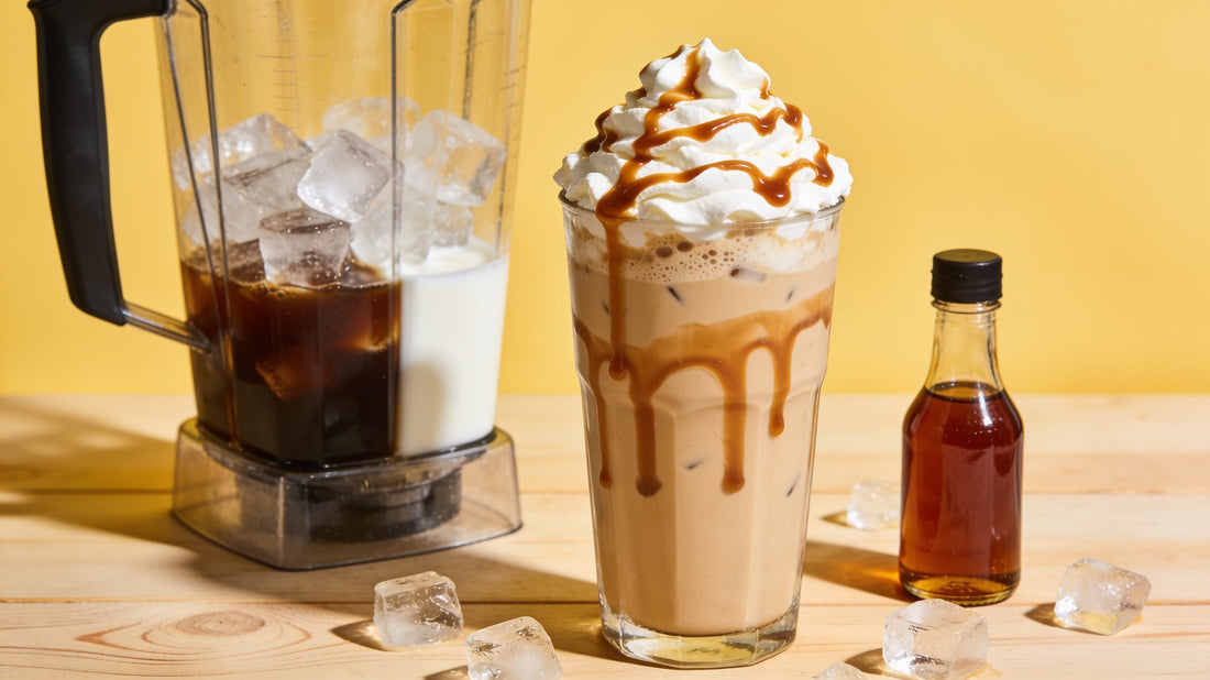 A caramel frappe topped with whipped cream and caramel drizzle beside a blender of coffee, milk and ice