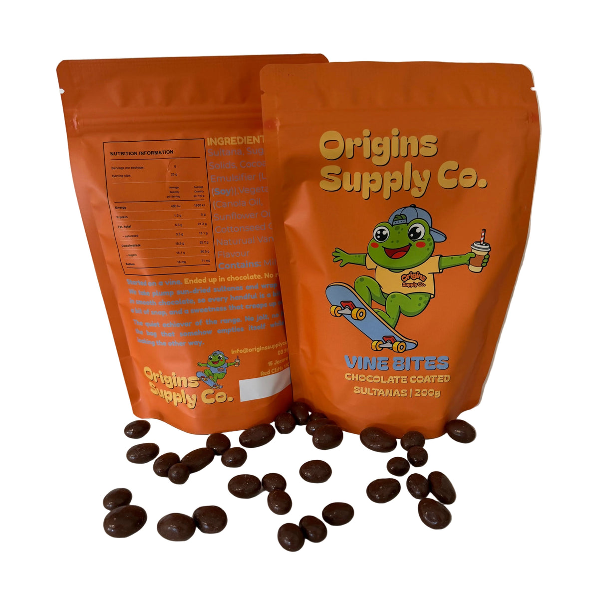 Two orange stand-up pouches of Origins Supply Co.  chocolate coated Sultanas, with several loose dark brown candy pieces scattered on a white marble countertop in front of them.