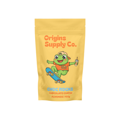 A yellow stand-up pouch of Origins Supply Co. Choc Rocks chocolate coated almonds, featuring a cartoon green frog character on a skateboard with an orange shirt and a blue skateboard.