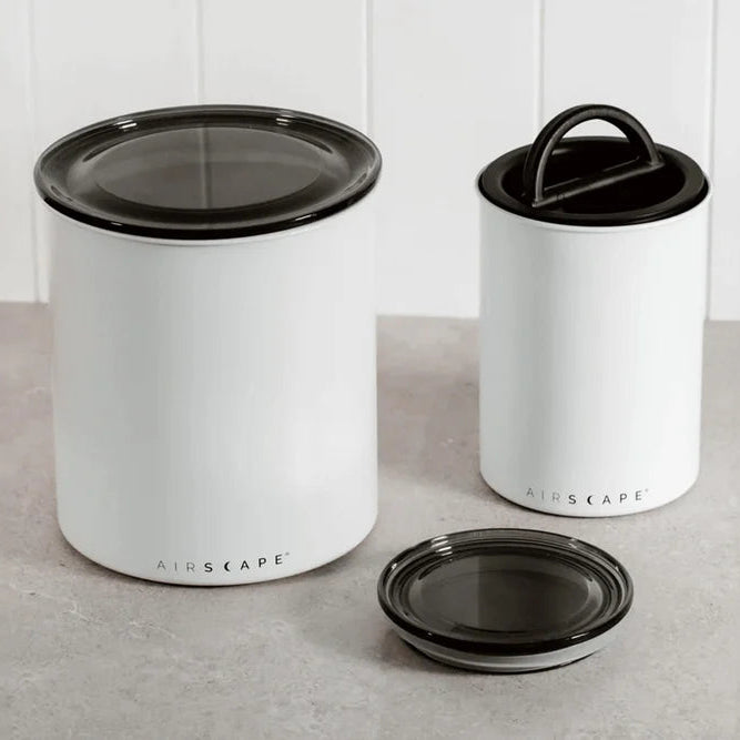 Two white containers with black lids on a light gray surface.