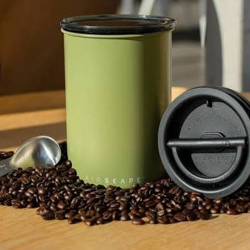 Green travel mug with black lid on coffee beans